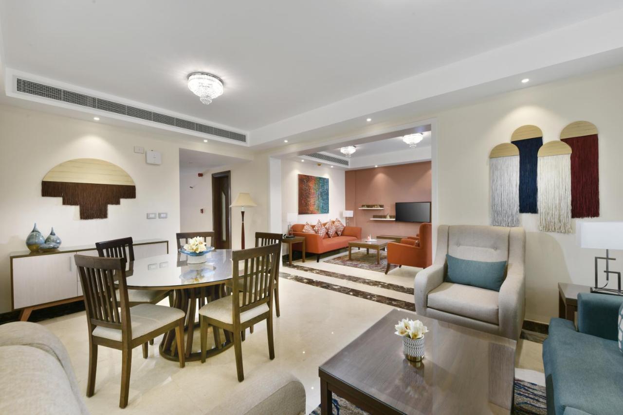 Tolip Resort El Galala Majestic Ain Suchna Exterior foto The photo shows a modern living room space that is elegantly designed. It features a seating area with a comfortable sofa and armchairs, complemented by a decorative coffee table. There is a dining table with several wooden chairs, providing a cozy a