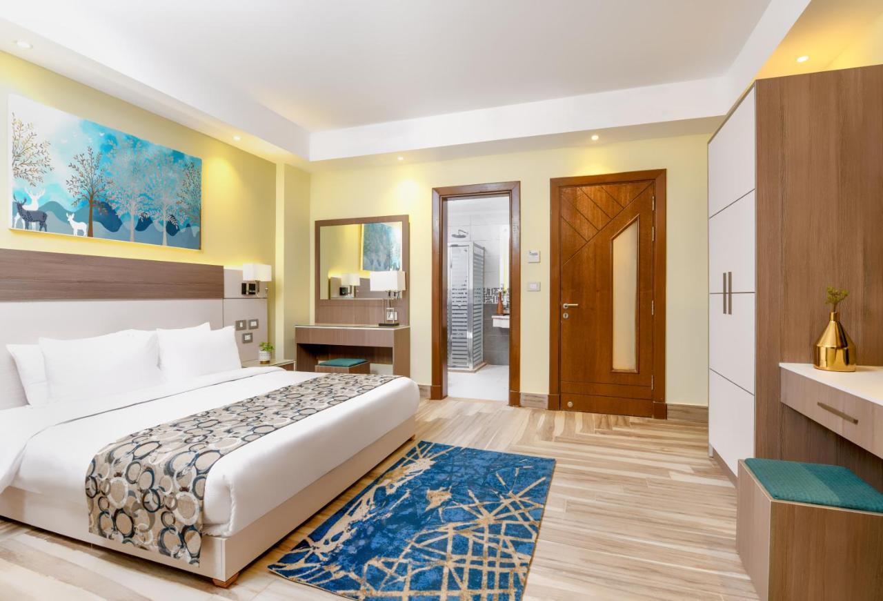 Tolip Resort El Galala Majestic Ain Suchna Exterior foto The photo shows a well-decorated hotel room. There is a large bed with white linens and a decorative throw blanket. The room features a wooden wardrobe and a bedside table with lamps. A colorful rug is placed on the floor, adding warmth to the space.